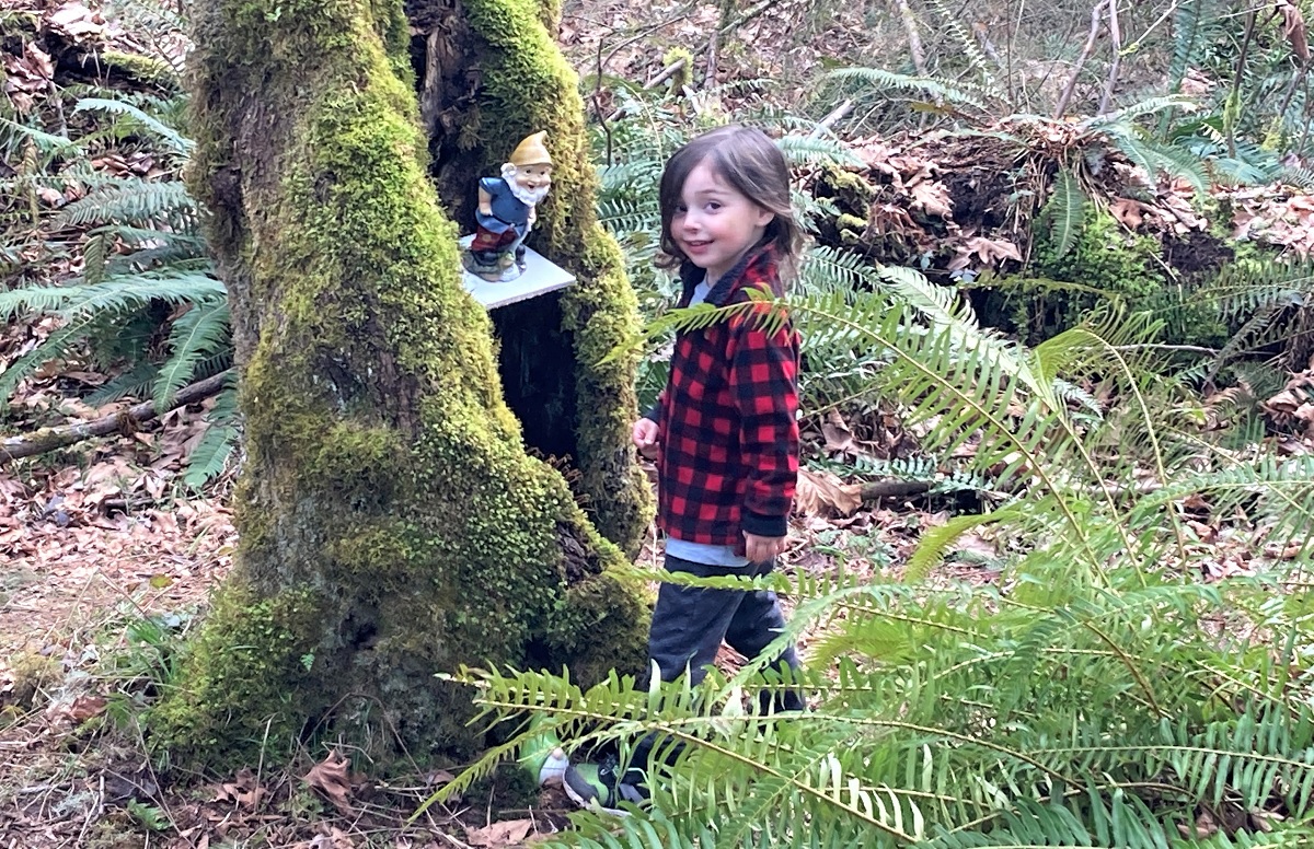 Kid in plaid jacket standing by gnome in tree along Maple Valley gnome trail fun for Seattle-area families