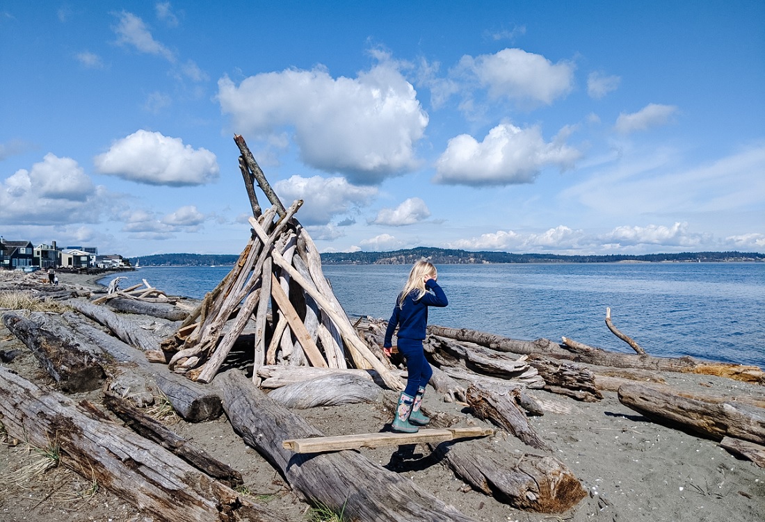 Girl on Bainbridge Island beach climbing on driftwood Explore Bainbridge spring break activity kit