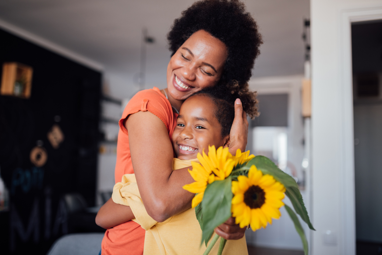 mother and daughter hugging with a vase of sunflowers on the kitchen table
