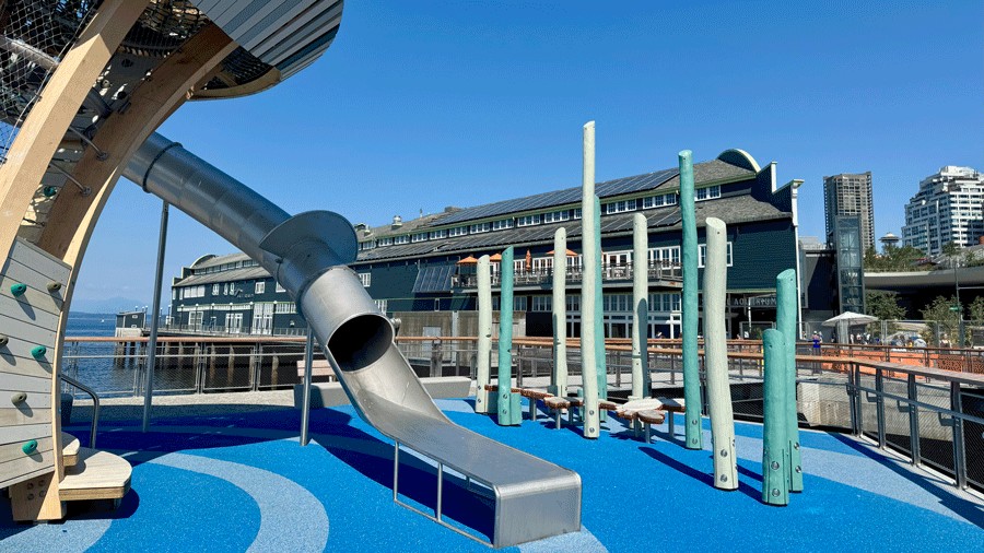 the 18-foot-high tube slide at Pier 58's new playground, with a kelp forest of climbing poles and the Seattle Aquarium behind it