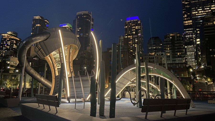 New Waterfront Park playground lit at night with city skyline behind it