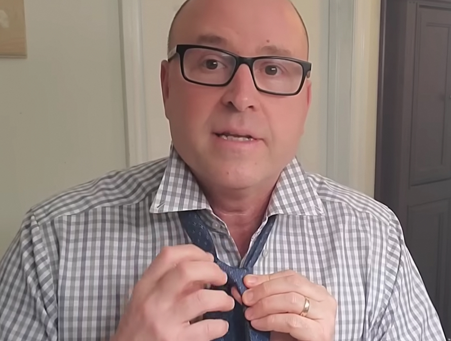 man looking into the camera tying a necktie