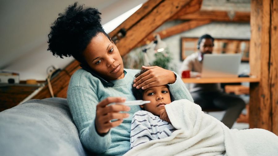mom with a sick child looking at their fever and calling the doctor