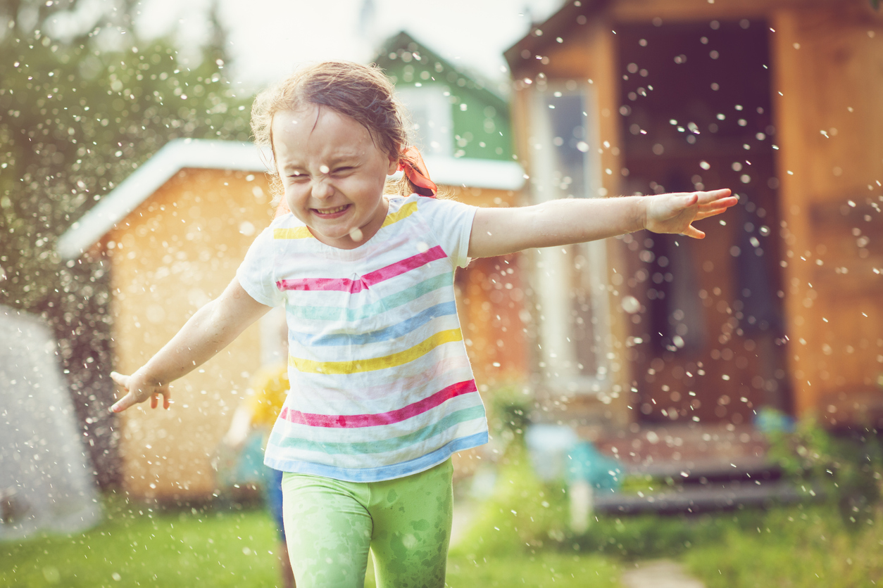 closeup of a girl running through a sprinkler with her arms out