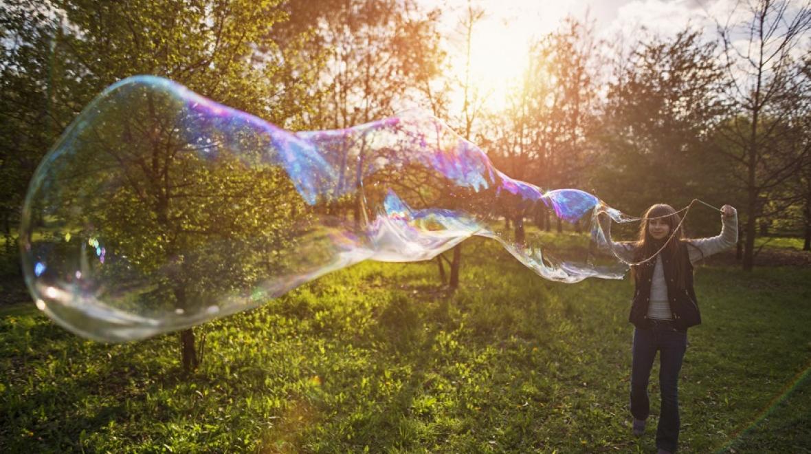 girl with her arms spread at sunset with a humongous bubble trailing in front of her