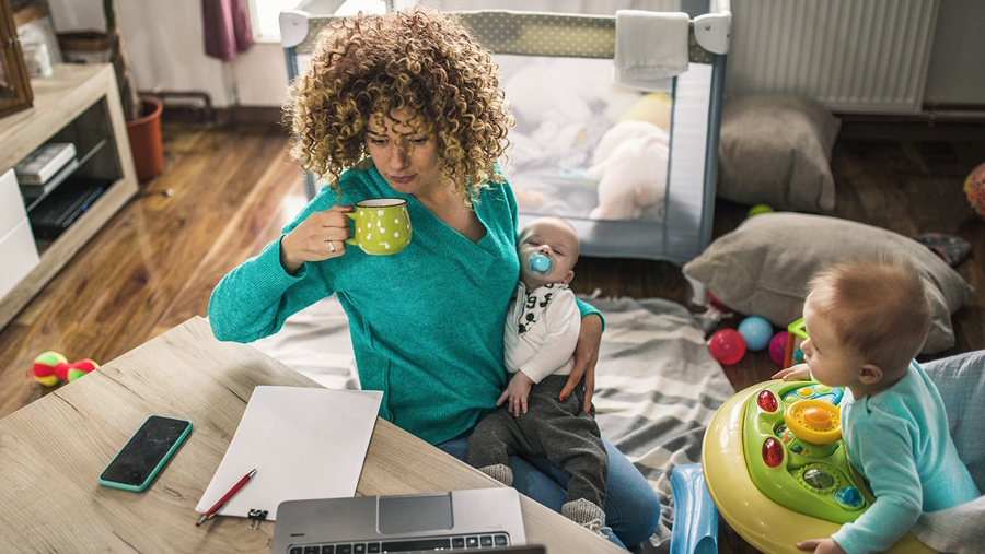mom working and holding baby with another baby nearby default parent