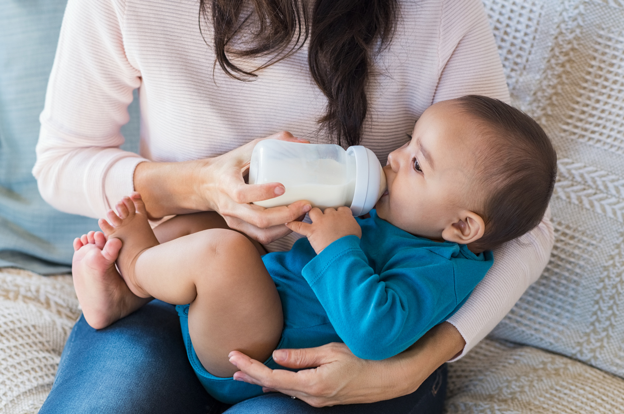 Baby drinking milk from bottle on his nanny's lap