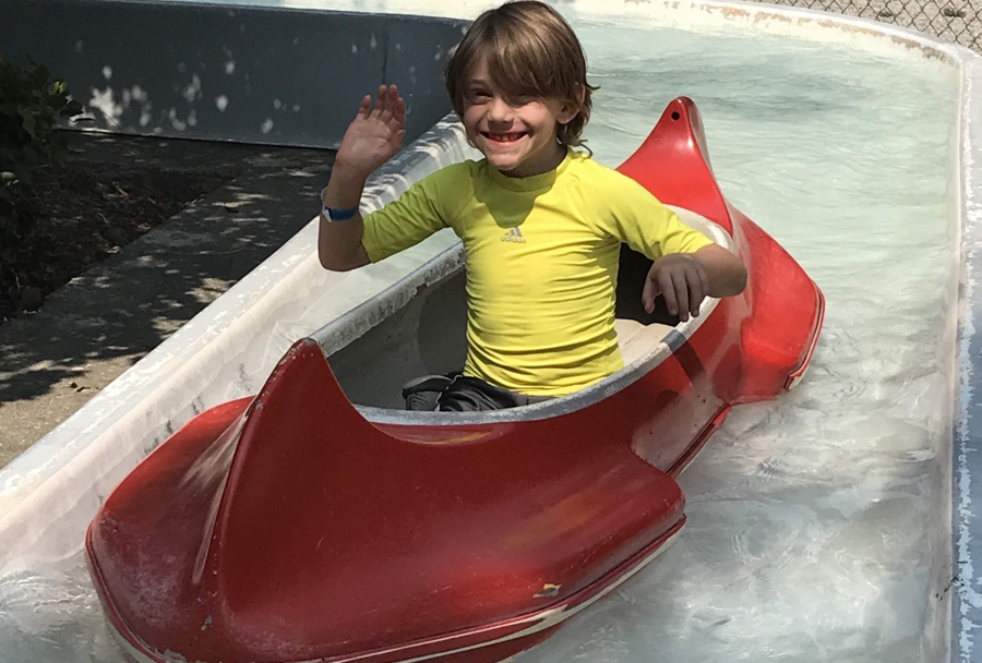 Boy in a yellow shirt riding in a red canoe at a theme park 