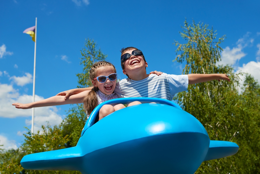 Brother and sister wearing sunglasses on an airplane ride at a theme park