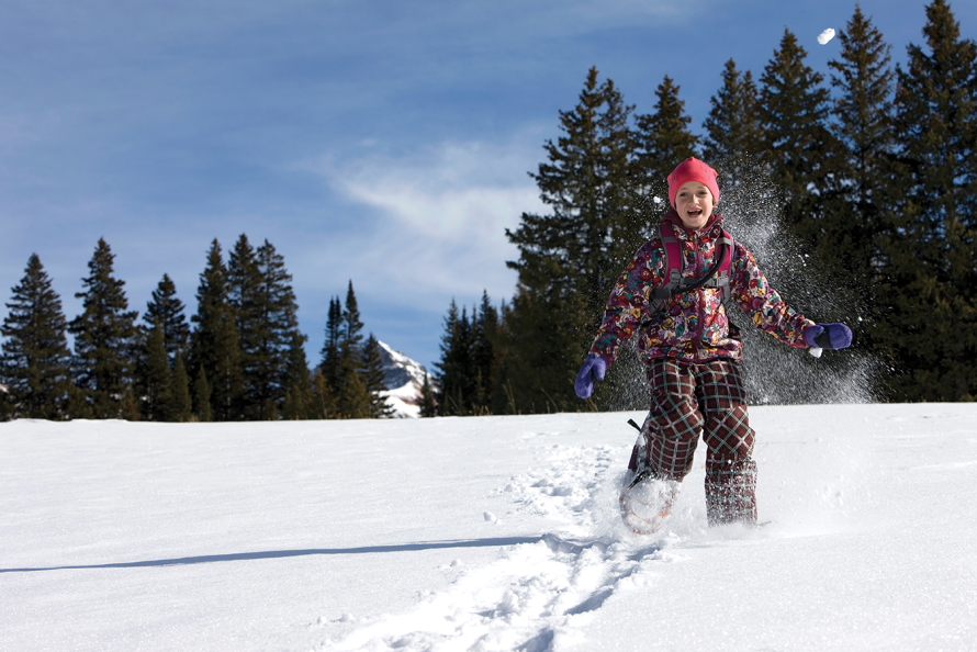 Child wearing a snowsuit running in a field of snow