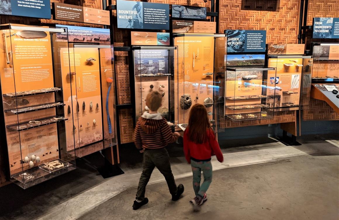Young kids at Seattle’s Burke Museum walking in front of a wall of natural history and culture exhibits