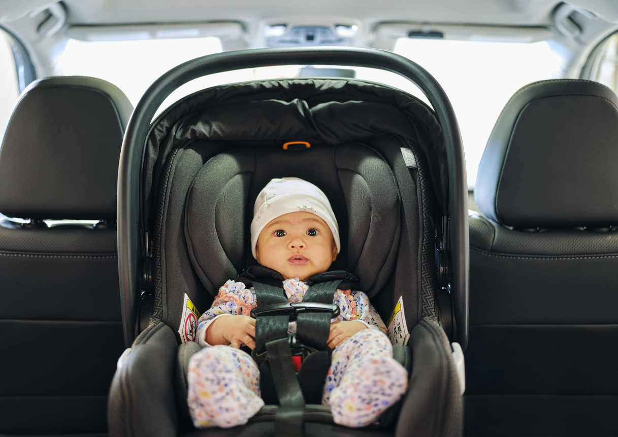 baby in a rear-facing, safety-stickered car seat in the backseat of a car