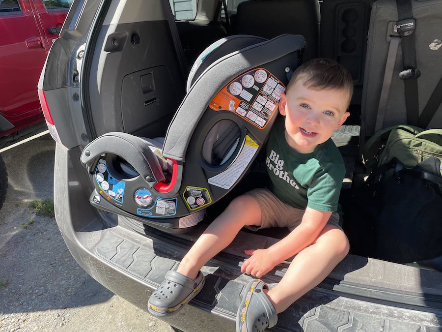 child sitting next to his carseat showing the safety labels required of all officially certified carseats