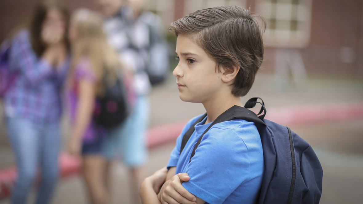 Boy standing alone next to a group of kids, ADHD and lacking social capital.
