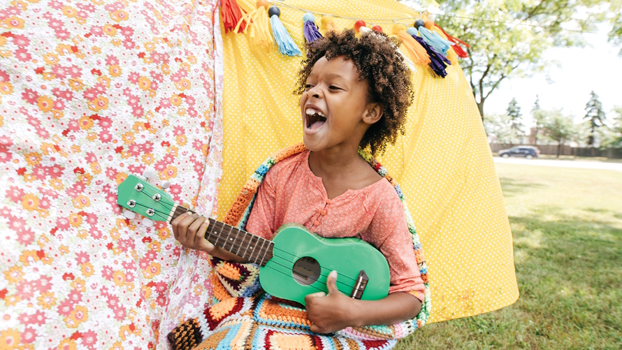 Kid playing a green guitar and singing at a performance arts summer camp