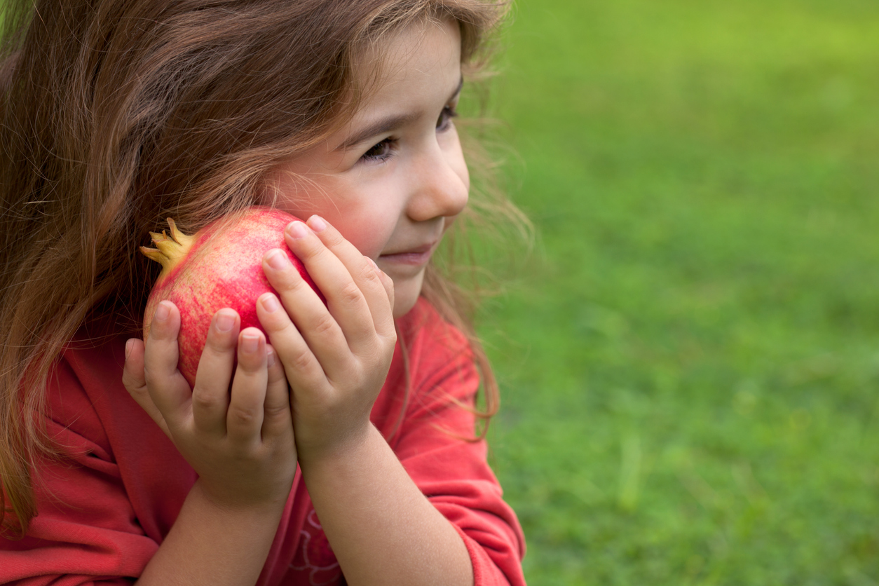 a girl holds a pomegranate to her cheek and smiles
