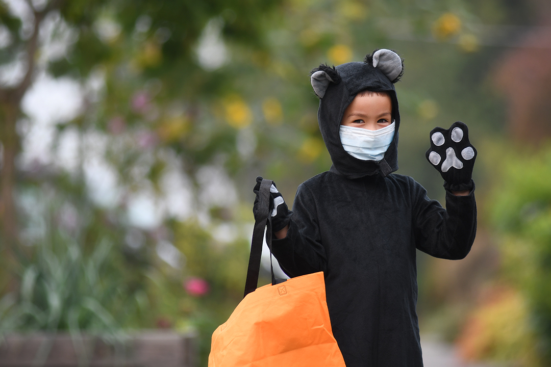 boy wearing a cat costume and mask waving at the camera outdoors Halloween 2020