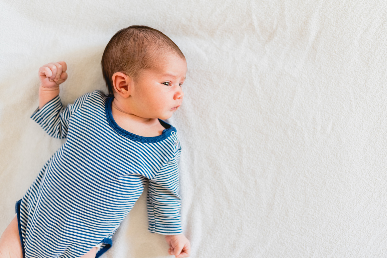 Adorable newborn baby in a long-sleeved striped onesie lying on her back in her crib