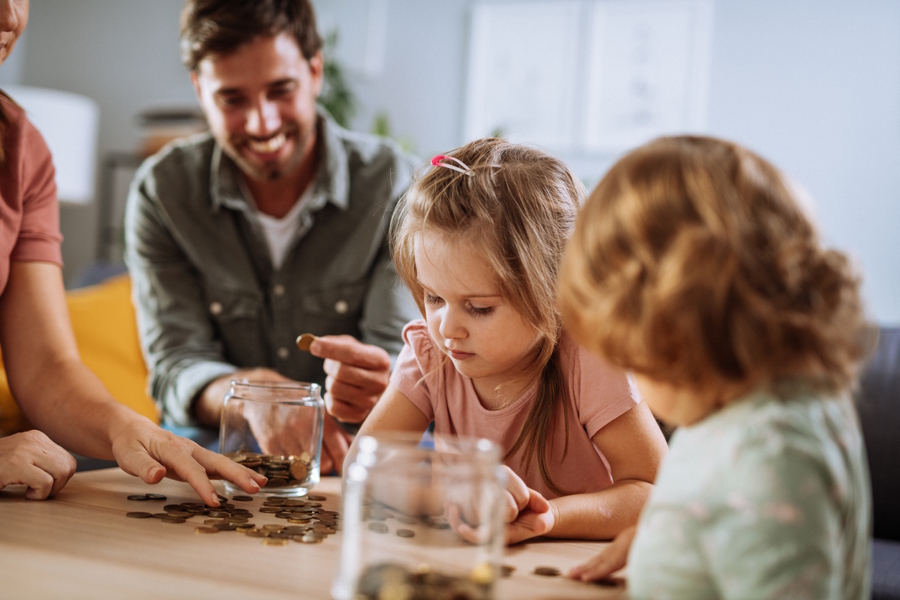 kids sorting money at home on a table with parents in the background