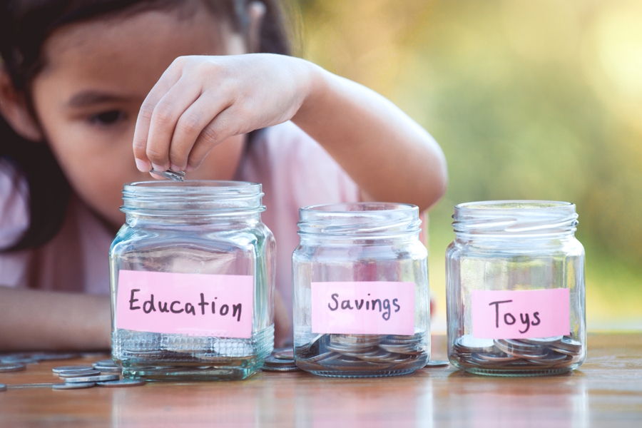 girl putting coins into jars labeled Education, Saving, and Toys