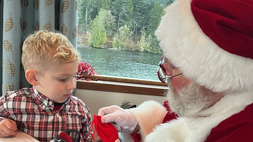 Young boy sitting next to Santa looking at a small red bag on a Coco cruise at Alderbrook Resprt
