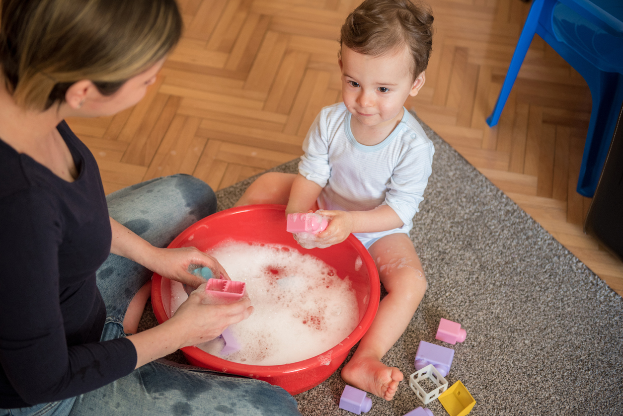 A mother and her toddler son make a game out of cleaning toys