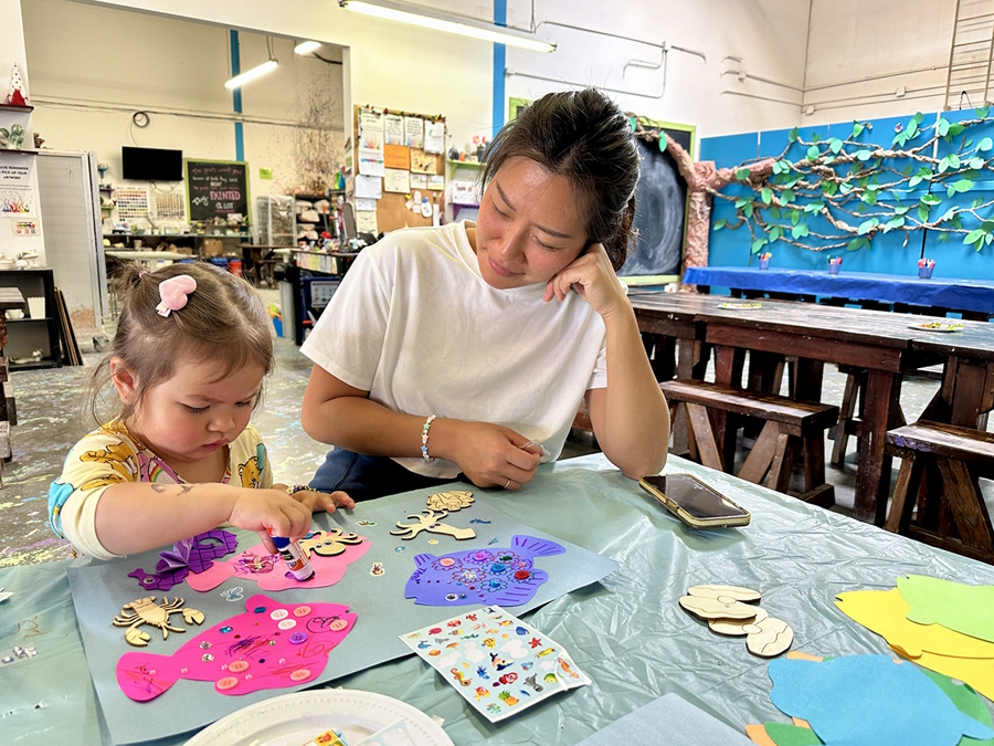 A little girl making an art project with paper, glue and wooden shapes is messy play