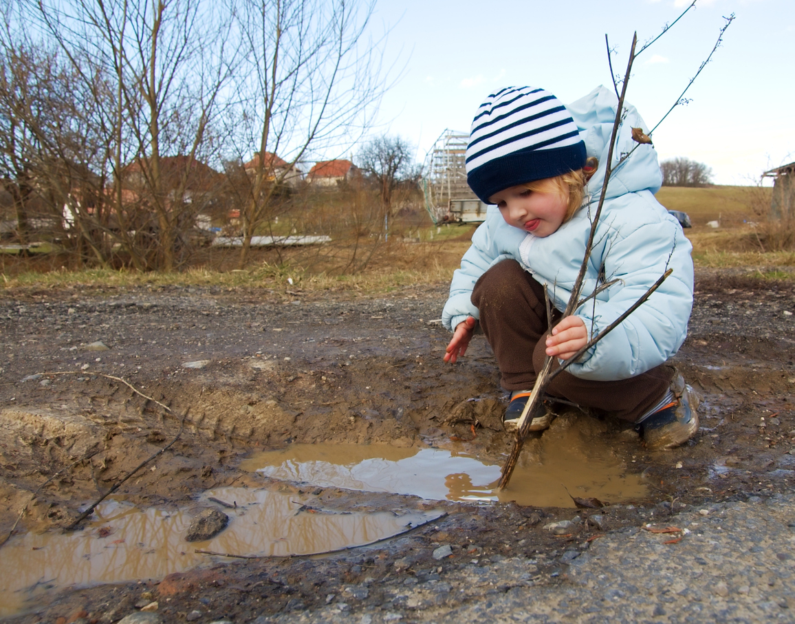 Girl playing with a stick in a mud puddle