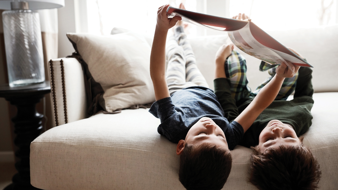 Brothers reading a book together on a couch upside-down