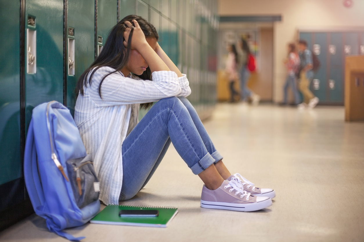 a frustrated student sits with head in hands in front of her locker, signs of toxic achievement culture