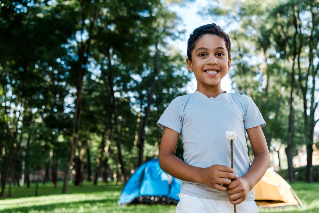 boy holding a marshmallow on a stick with two tents in the background