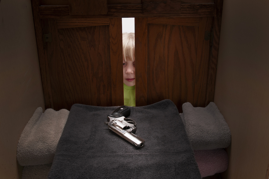 a child looking into a cabinet where a gun is kept