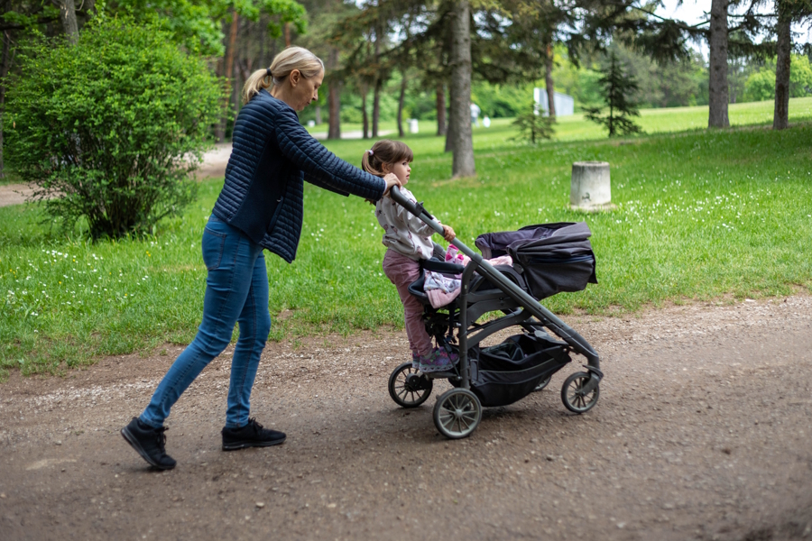 woman pushing a stroller with two children on a park path