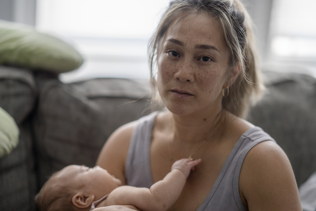 an overwhelmed mom looks into the camera while holding her baby