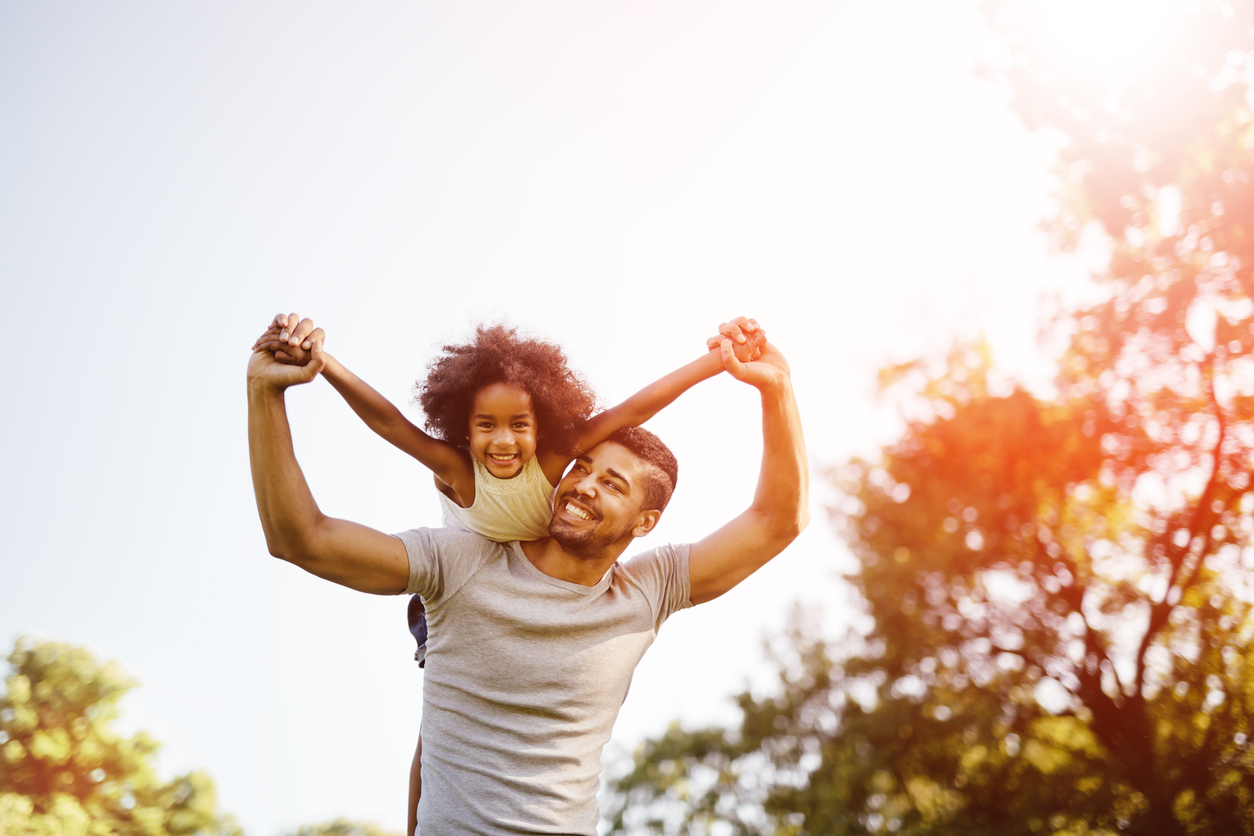 father with his daughter on his shoulders with their arms spread