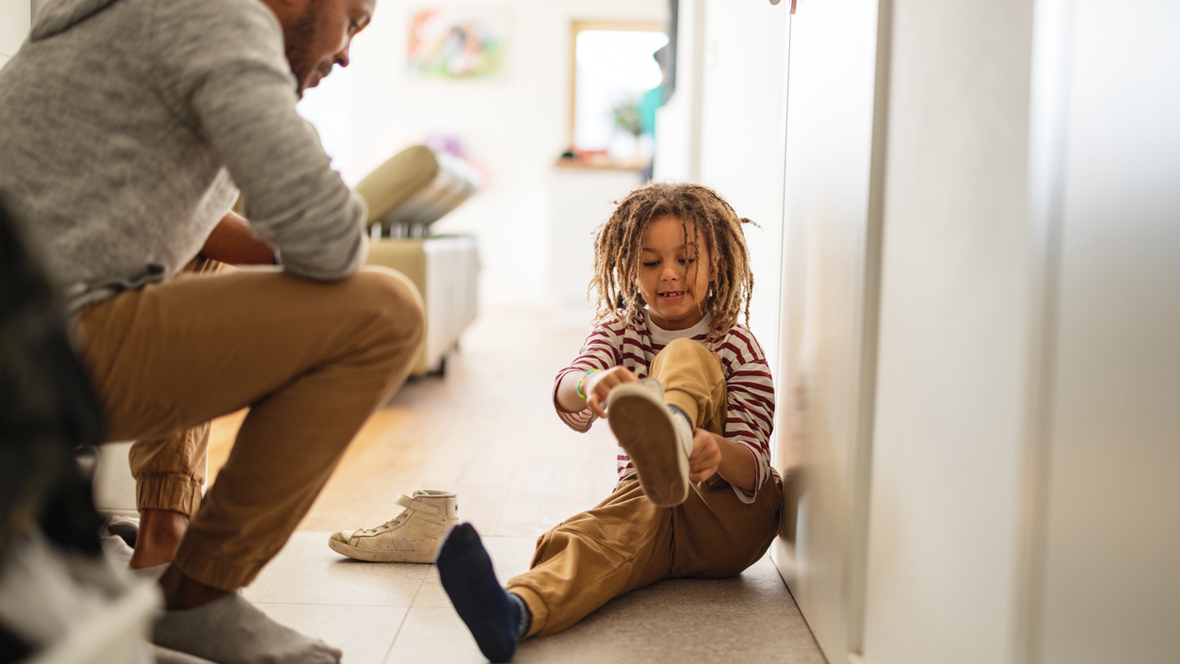 child putting on shoes while dad waits