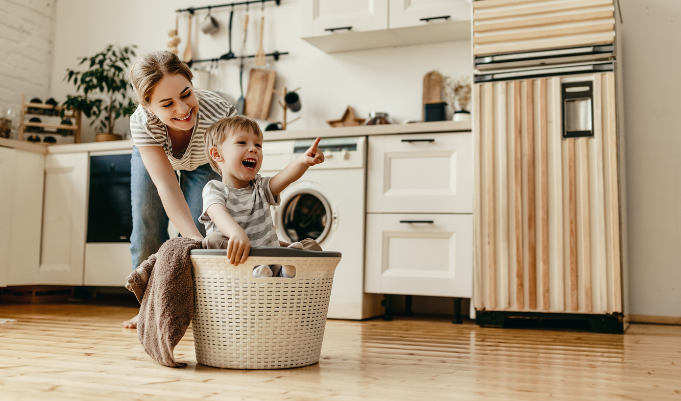 mom pushing her smiling son across the floor in a laundry basket