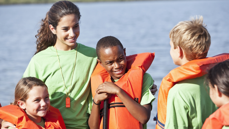 Teen girl who is a camp counselor standing with kids benefits of being a camp counselor