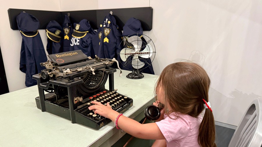 young child playing on an antique typewriter at a themed indoor playground with a pretend police station