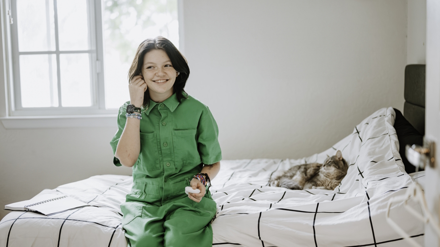 nonbinary youth sitting on a bed with a cat