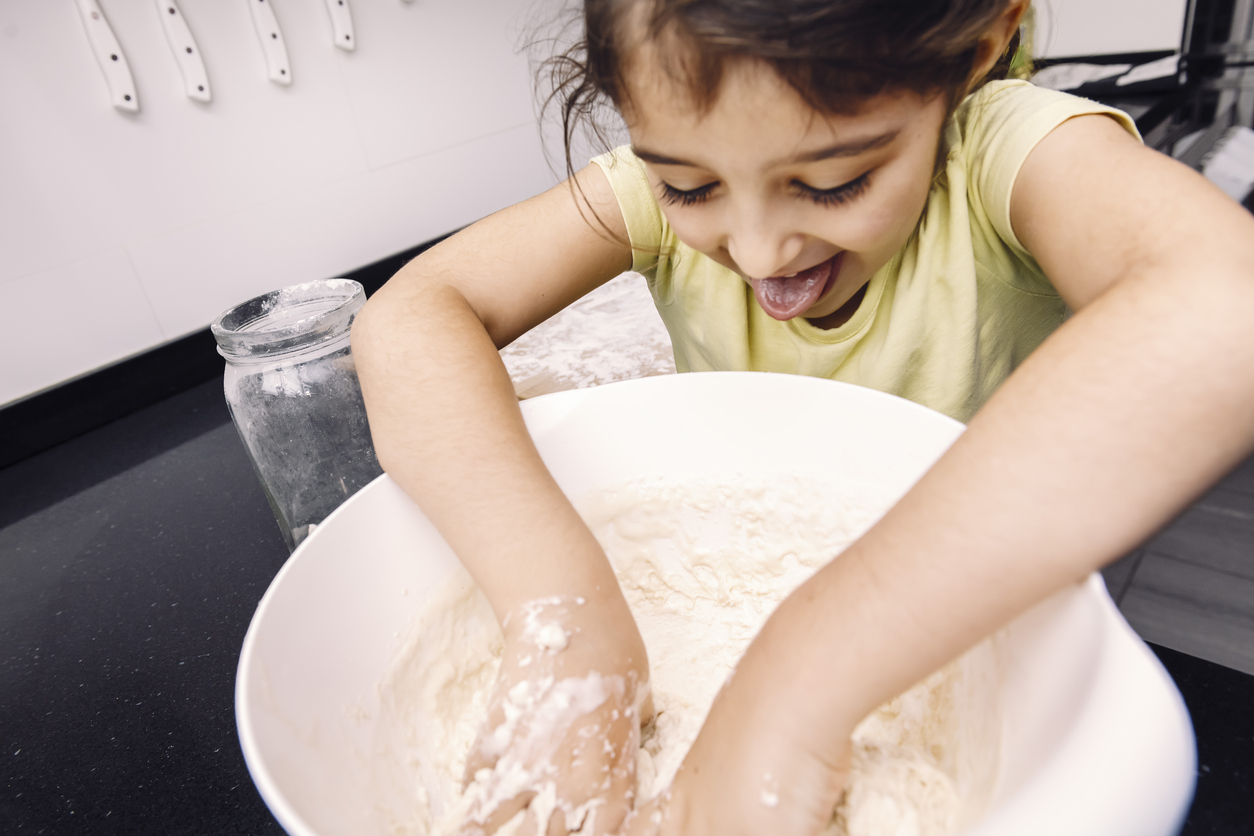 Cute little girl sticks her tongue out as she mixes flour in a bowl