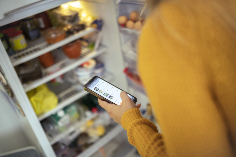 Person standing in front of an open refrigerator shopping for groceries online