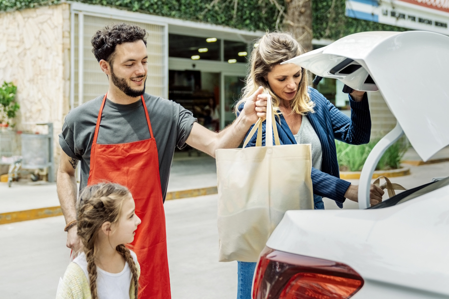 Man helping woman and little girl load groceries that were bought online into the back of a car