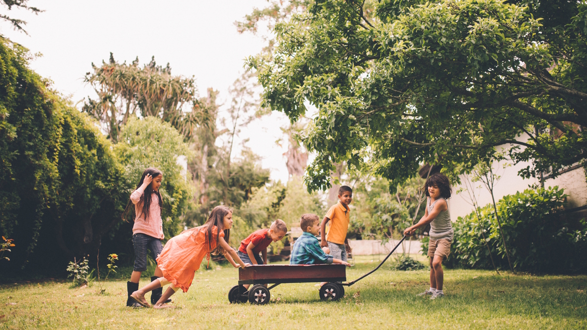 group of kids playing with a wagon in a yard in the summer