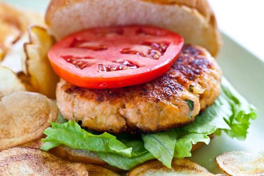 salmon burger on a plate with a slice of tomato and lettuce on a bun summer burger recipe