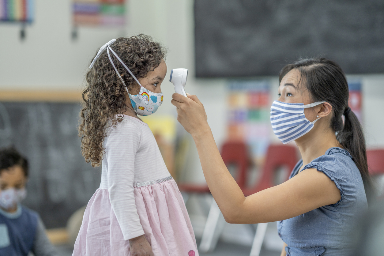 daycare woman in a mask taking a child's temperature