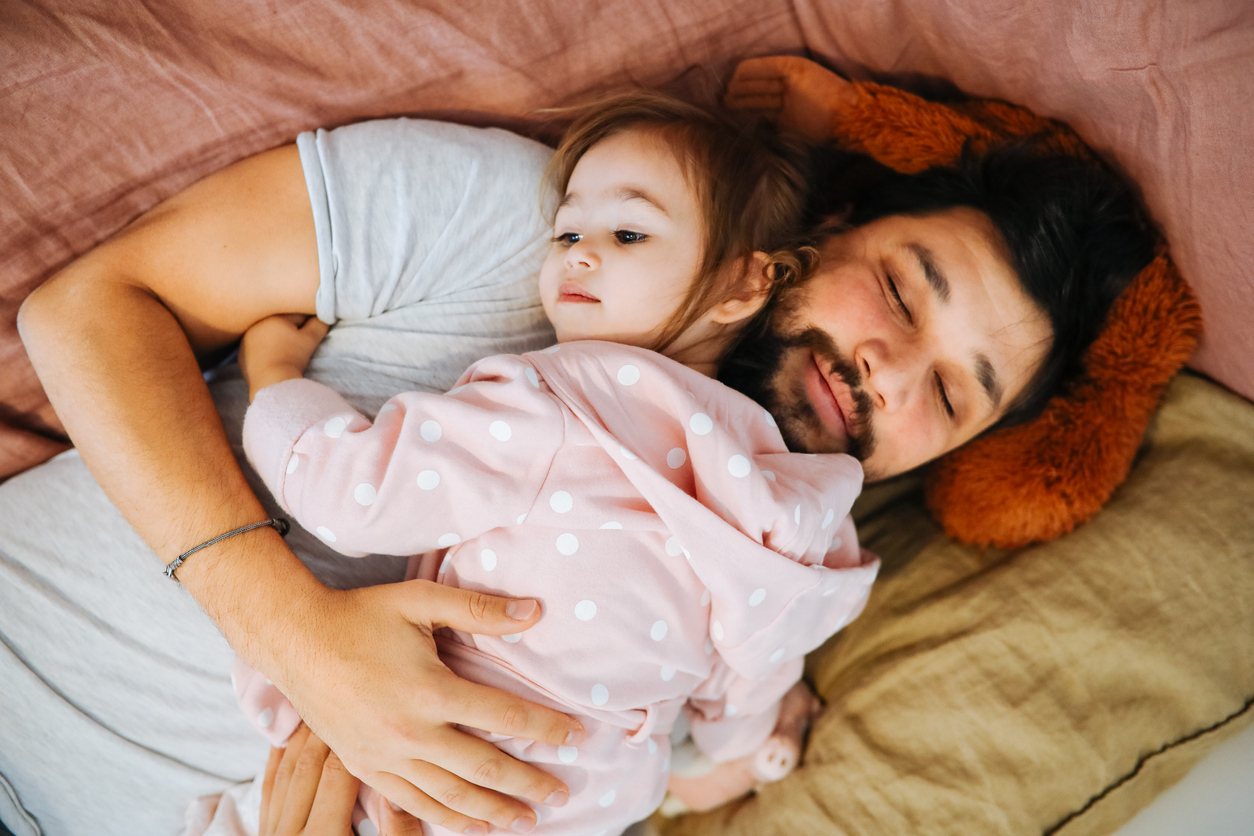 topdown view of a father and daughter snuggled up on multicolored blankets