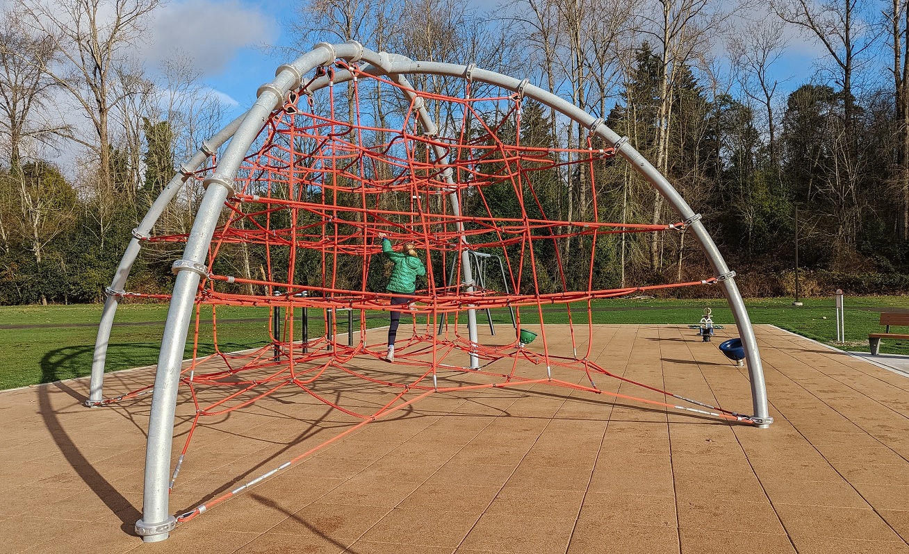A young girl in a green jacket climbs on the large rope dome climber at South Seattle area's new playground at Skyway Park