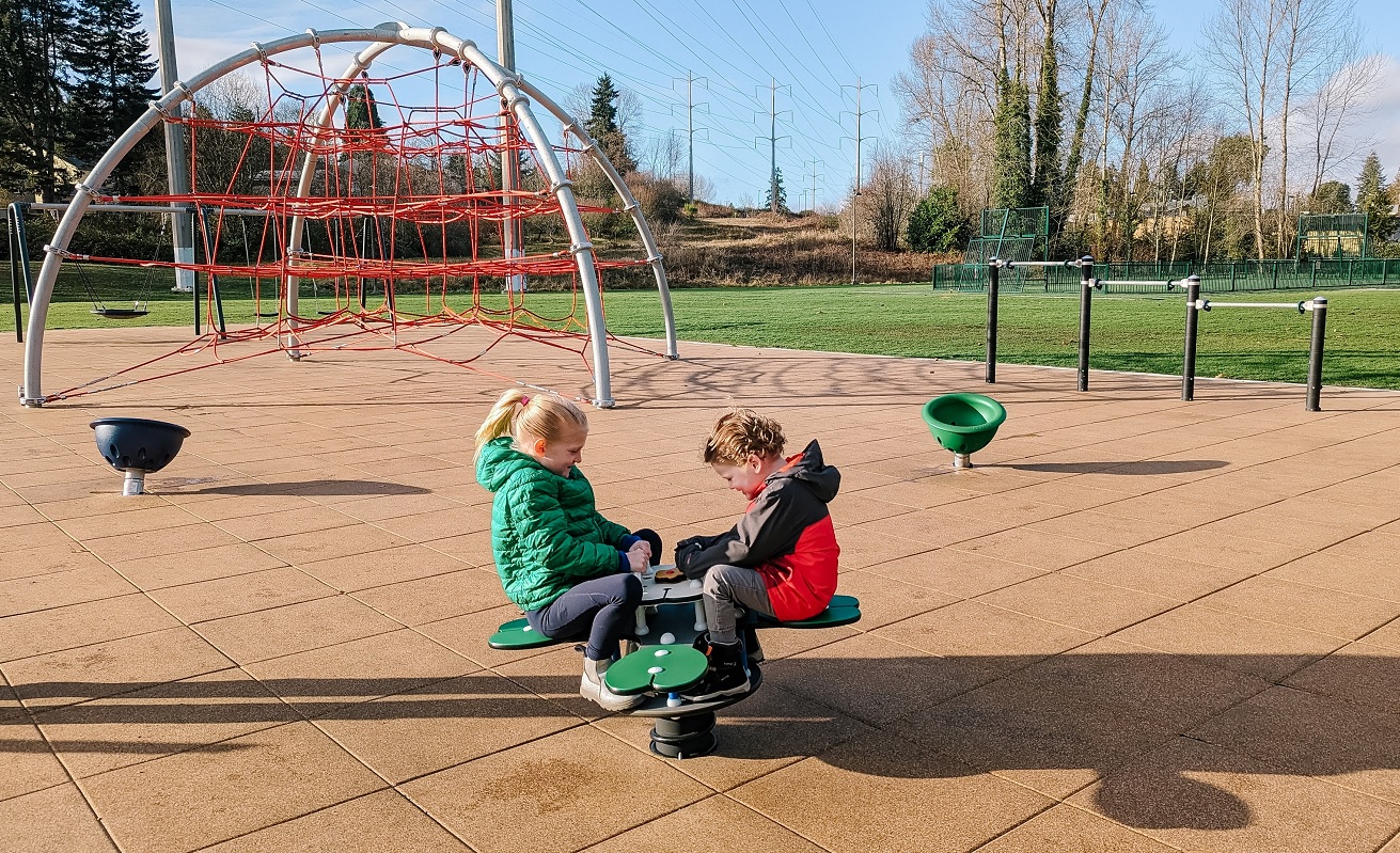 Laughing kids in winter jackets on a cold sunny day play on a seesaw bouncer at the new playground at South Seattle area's Skyway Park