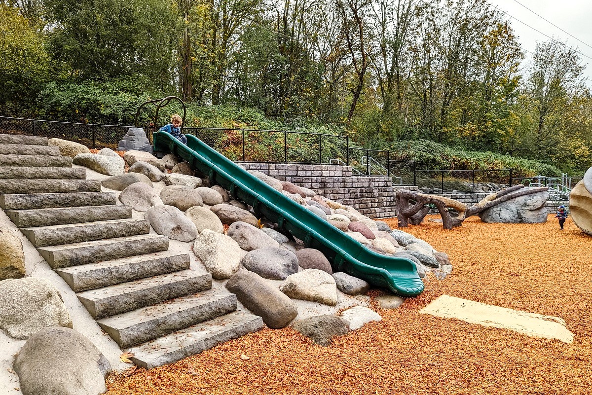 Young boy on the green hillside slide at Newport Hills Woodlawn Park’s new playground in South Bellevue